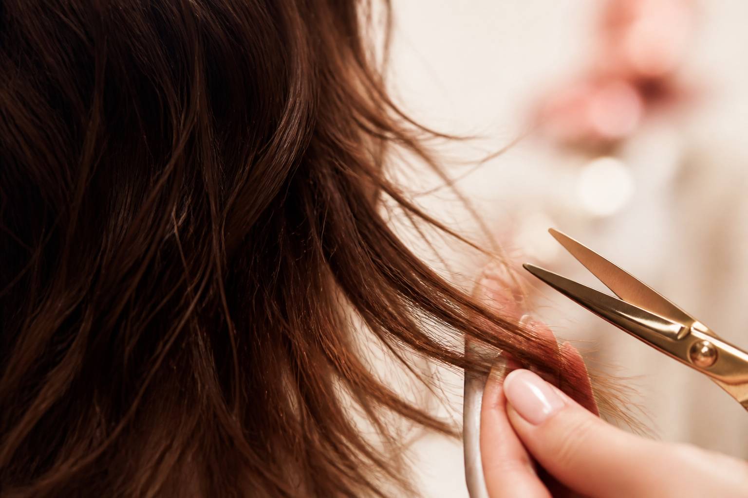 Pointes de cheveux bruns au carré déstructuré avec mèches effilées, main de coiffeuse et ciseaux